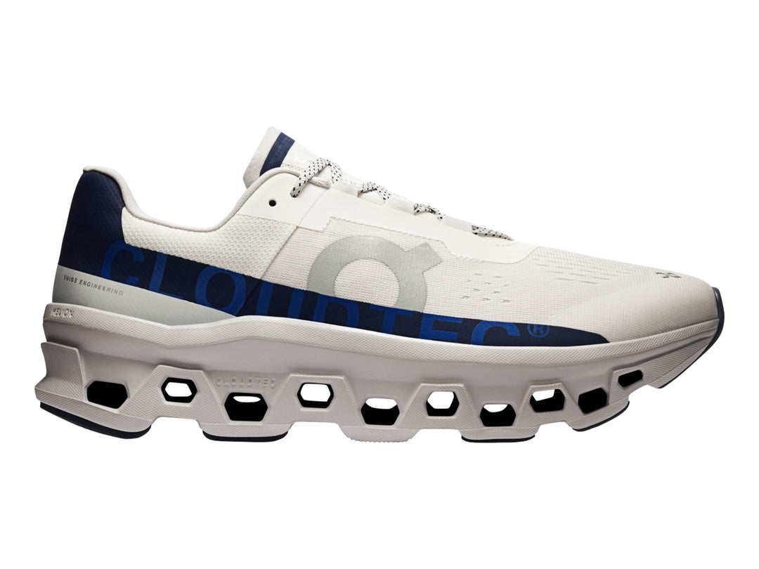 Tenis deportivos ON Cloudmonster en color marfil con detalles en azul marino y suela blanca estructurada.