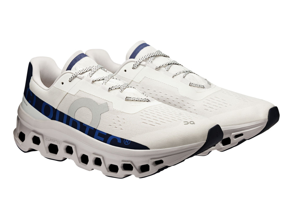 Tenis deportivos ON Cloudmonster en color marfil con detalles en azul marino y suela blanca estructurada.
