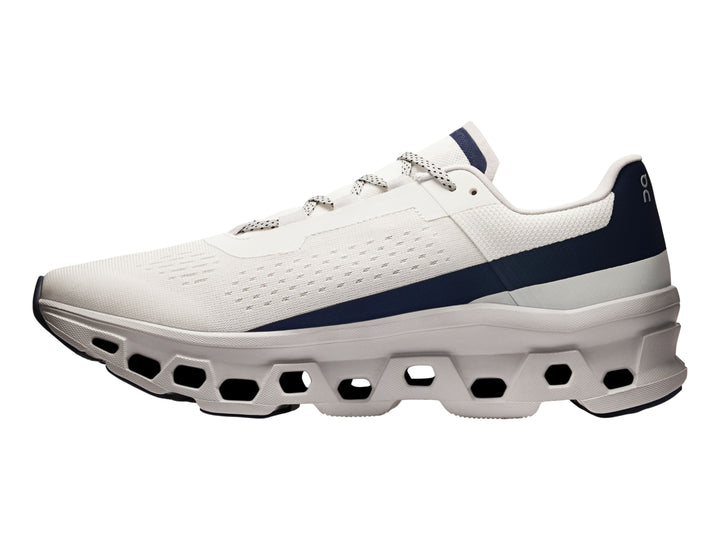 Tenis deportivos ON Cloudmonster en color marfil con detalles en azul marino y suela blanca estructurada.