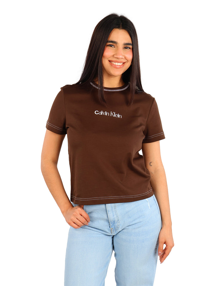 Mujer vistiendo una camiseta ajustada color café de Calvin Klein con costuras blancas contrastantes.