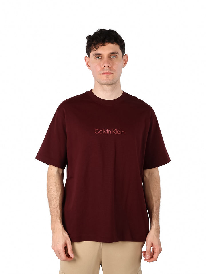 Hombre vistiendo una camiseta de manga corta color marrón oscuro con el logo de Calvin Klein en el pecho.