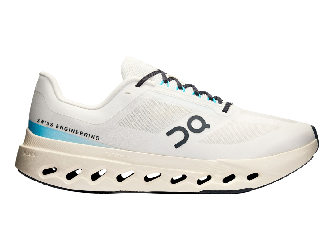 Tenis deportivos On Cloudsurfer Next en color marfil con detalles en azul claro y suela blanca perforada.