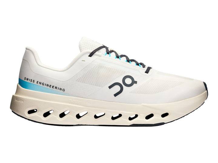 Tenis deportivos On Cloudsurfer Next en color marfil con detalles en azul claro y suela blanca perforada.