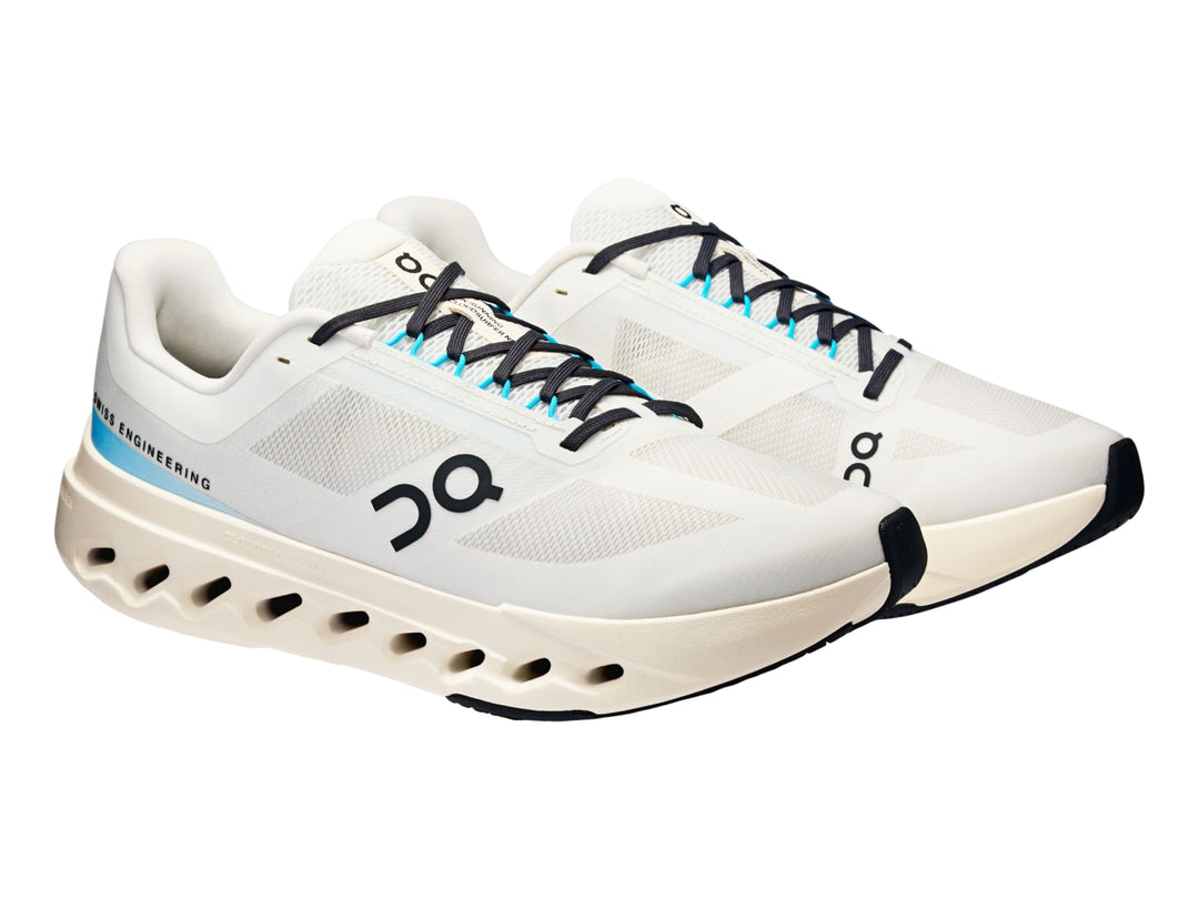 Tenis deportivos On Cloudsurfer Next en color marfil con detalles en azul claro y suela blanca perforada.