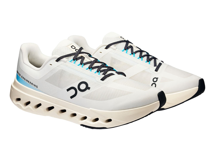 Tenis deportivos On Cloudsurfer Next en color marfil con detalles en azul claro y suela blanca perforada.