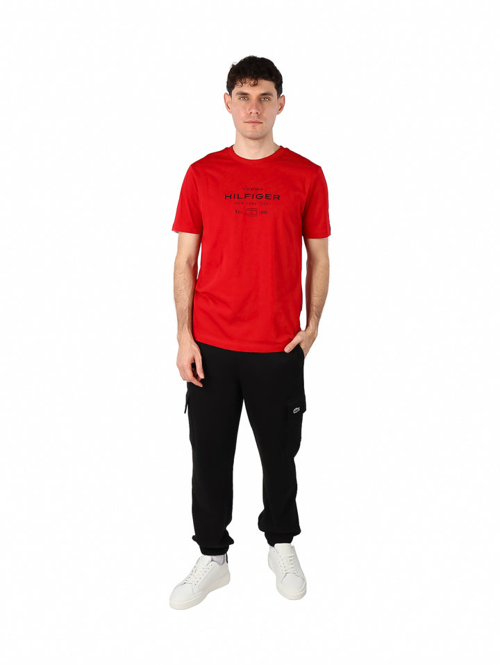 Hombre vistiendo una camiseta roja de manga corta con logotipo de Tommy Hilfiger en el pecho.