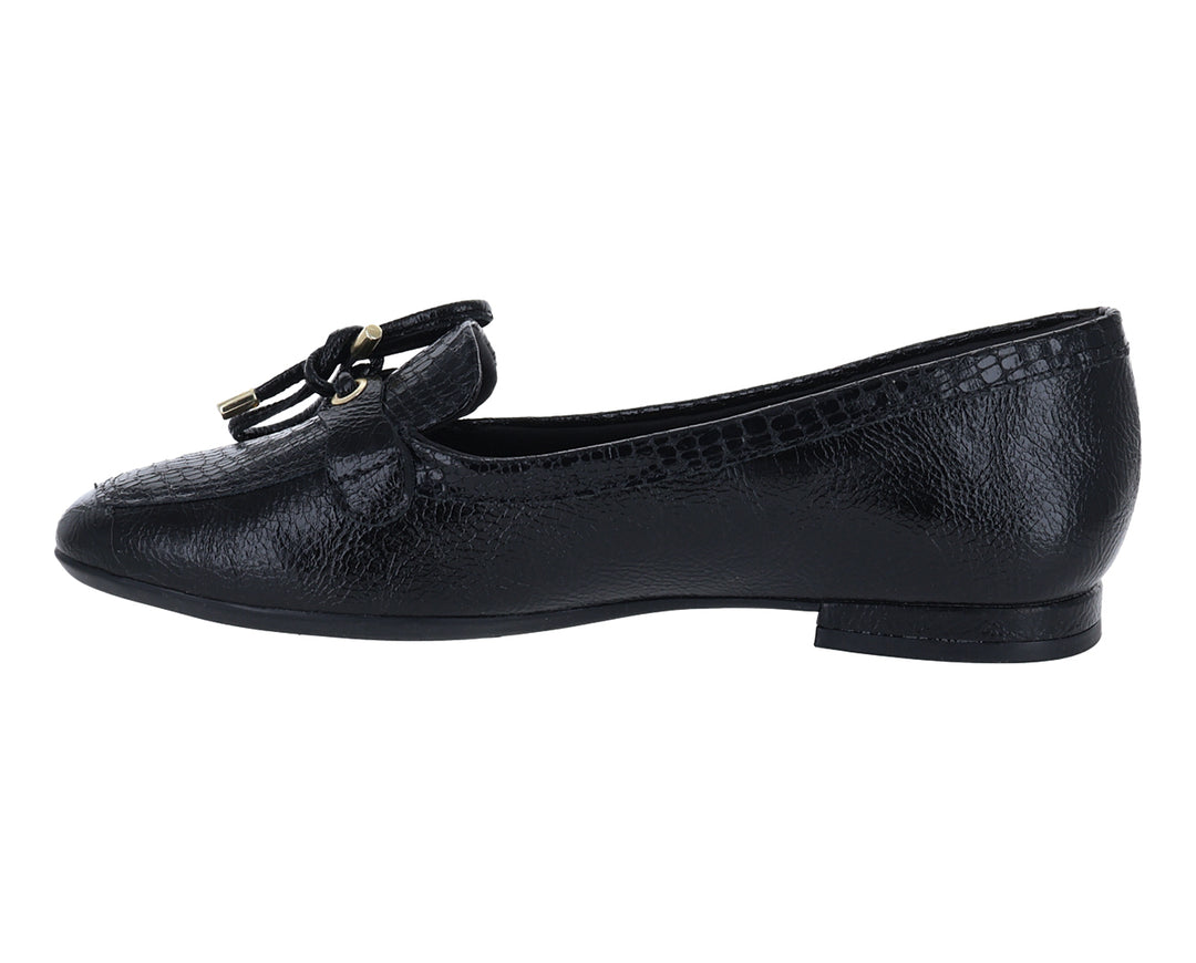 Mocasín negro para mujer con textura granulada y detalle de moño dorado en la parte superior.