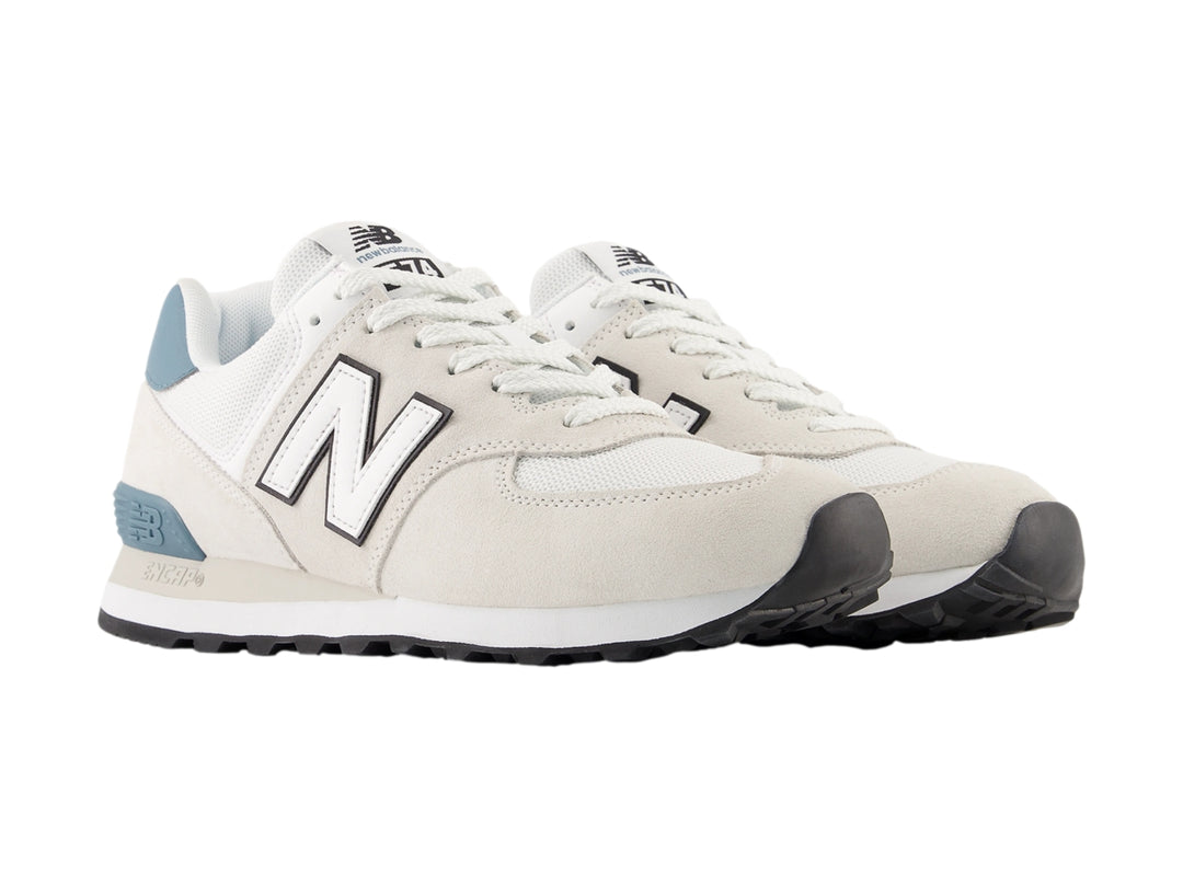 Tenis New Balance 574 para mujer en color gris claro con detalles en azul y suela blanca.
