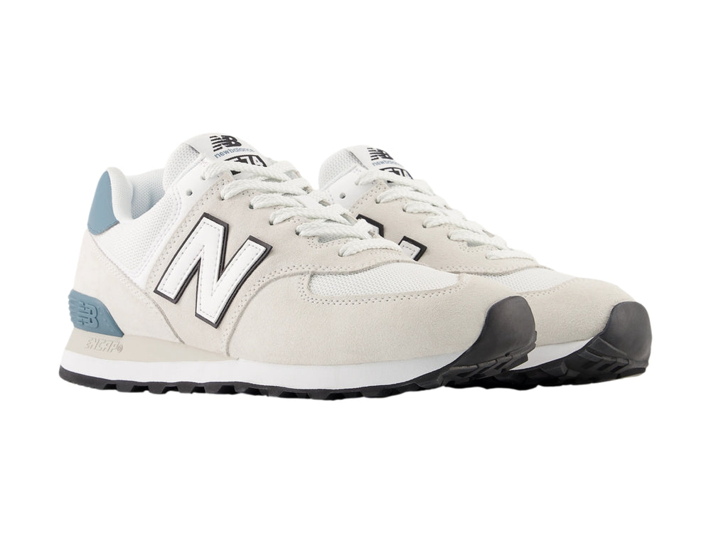Tenis New Balance 574 color gris claro con detalles en azul y suela blanca para hombre.
