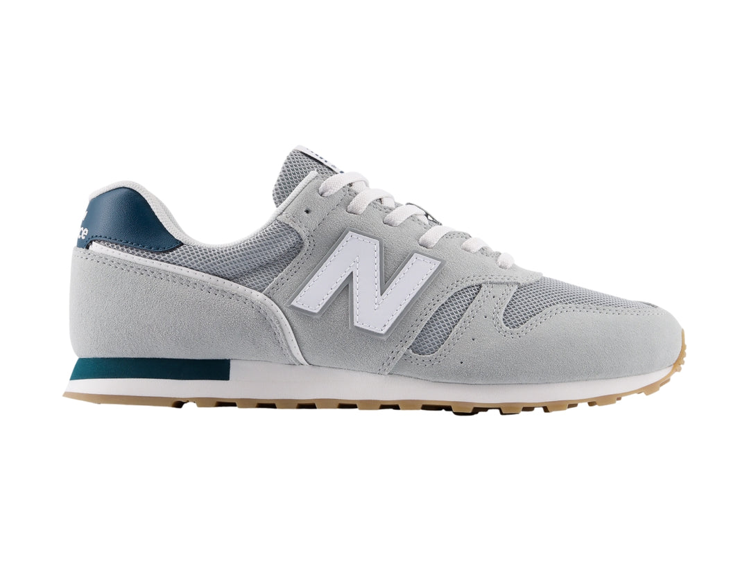 Tenis New Balance modelo 373 en color gris con detalles en blanco y azul marino, vista lateral.