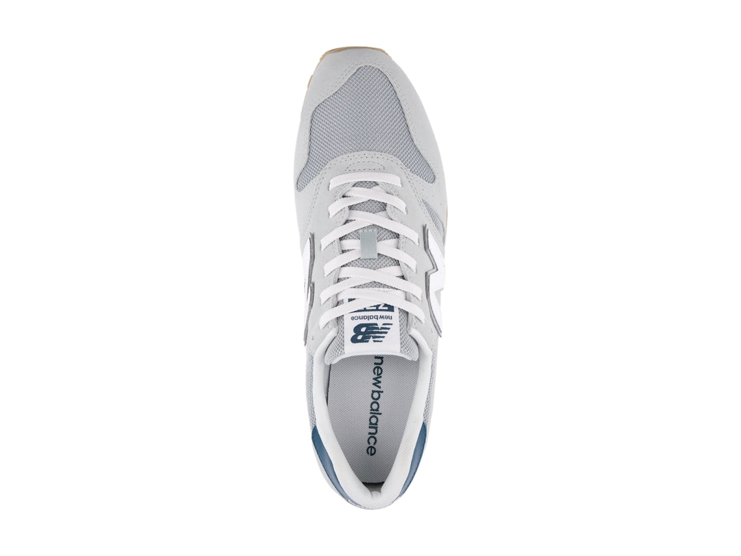 Tenis New Balance modelo 373 en color gris con detalles en blanco y azul marino, vista lateral.