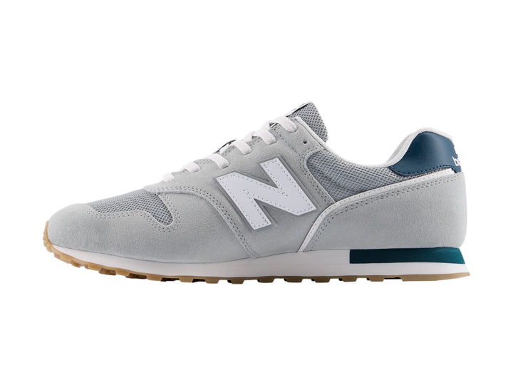 Tenis New Balance modelo 373 en color gris con detalles en blanco y azul marino, vista lateral.