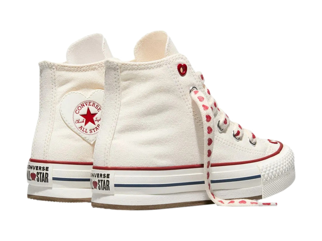 Tenis Converse blancos de bota alta con plataforma, agujetas decoradas con corazones rojos y detalles en rojo y azul.