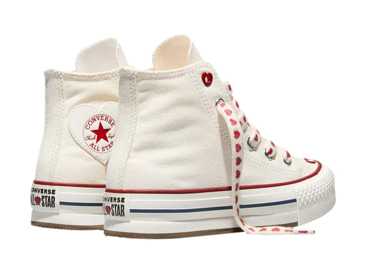 Tenis Converse blancos de bota alta con plataforma, agujetas decoradas con corazones rojos y detalles en rojo y azul.
