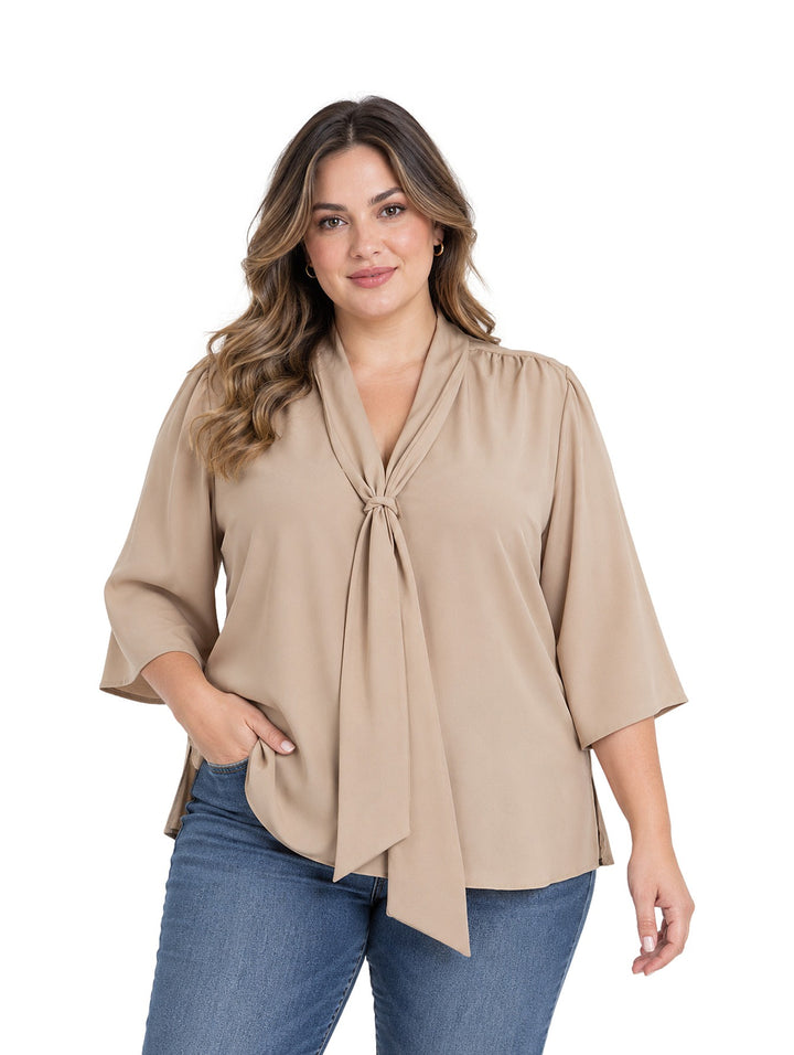 Mujer vistiendo blusa color taupe de corte curvy con cuello anudado y mangas tres cuartos.