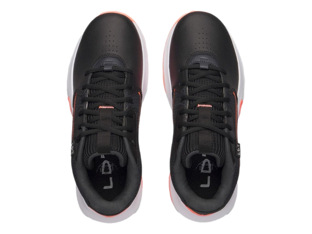 Tenis de baloncesto Under Armour color negro con detalles en naranja y suela blanca.