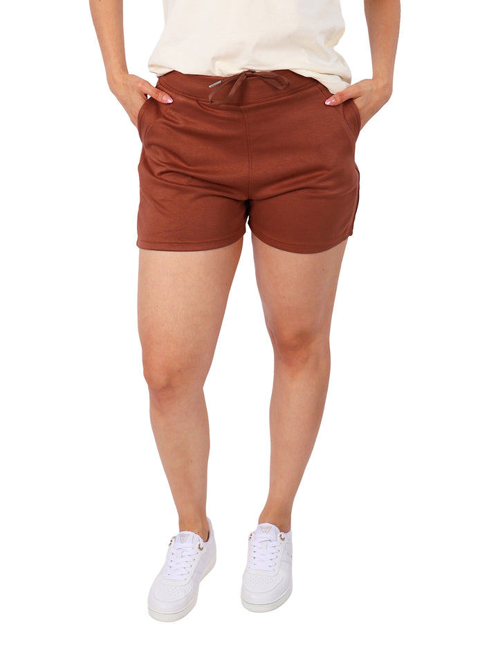 Mujer vistiendo shorts deportivos color marrón con bolsillos y cintura elástica.
