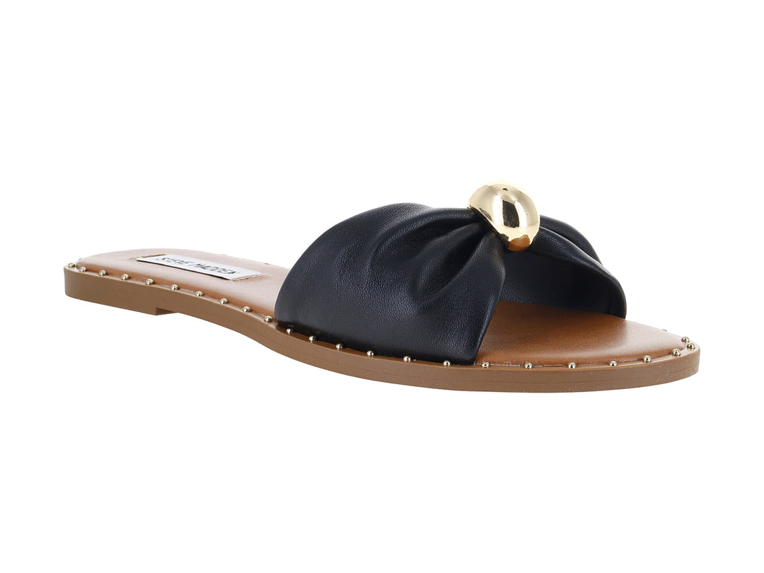 Sandalia plana Steve Madden color negro con detalle circular dorado en la parte superior y suela beige.