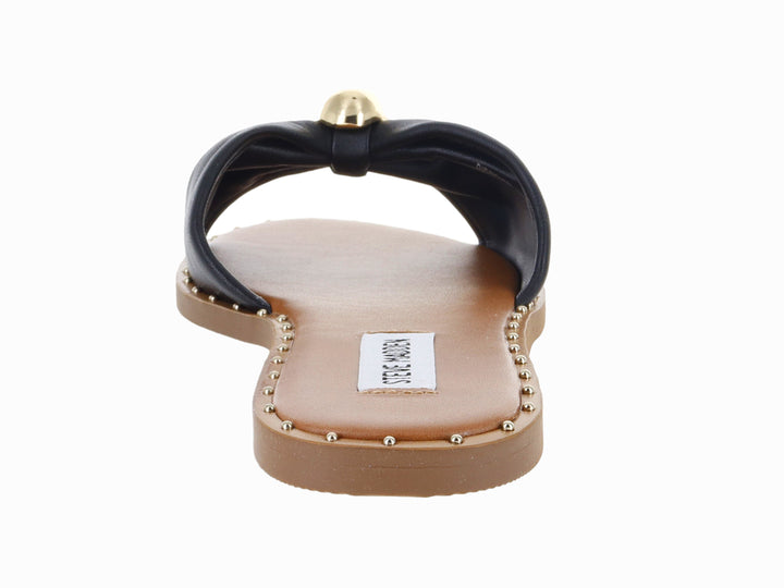 Sandalia plana Steve Madden color negro con detalle circular dorado en la parte superior y suela beige.