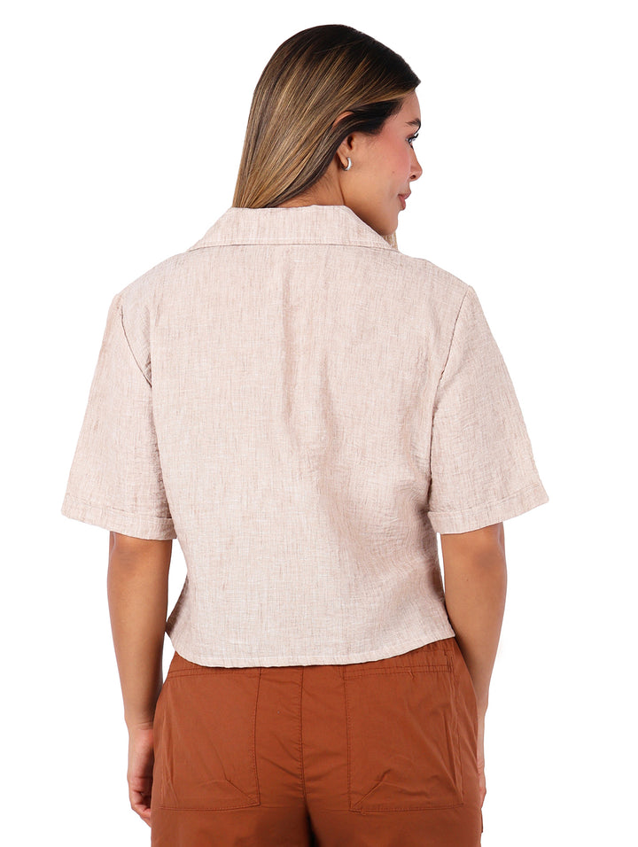 Mujer vistiendo una blusa camisera de color beige con manga corta y botones frontales.