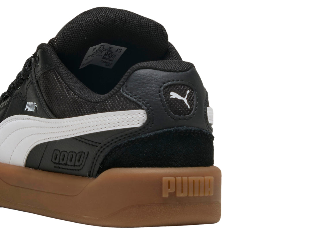 Tenis PUMA negros para niños con suela color café y franja blanca lateral.
