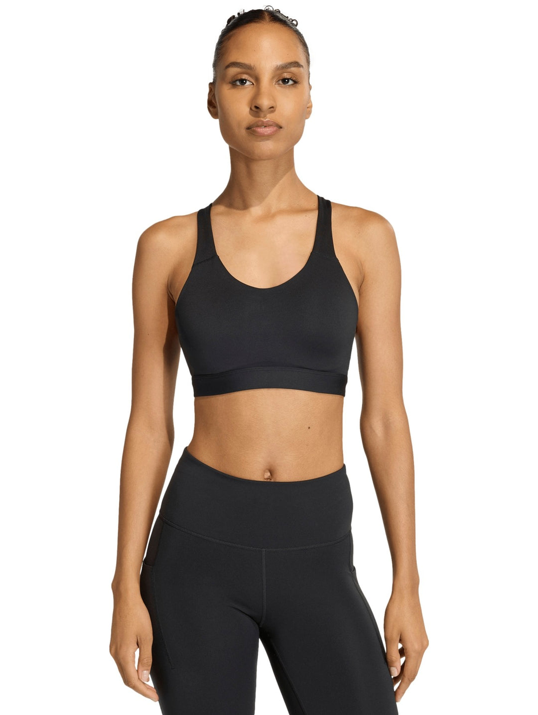 Mujer vistiendo un top deportivo corto color negro de la marca Adidas sobre fondo blanco.