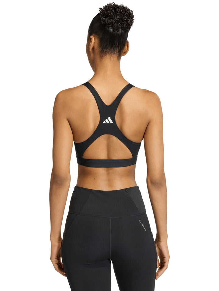 Mujer vistiendo un top deportivo corto color negro de la marca Adidas sobre fondo blanco.
