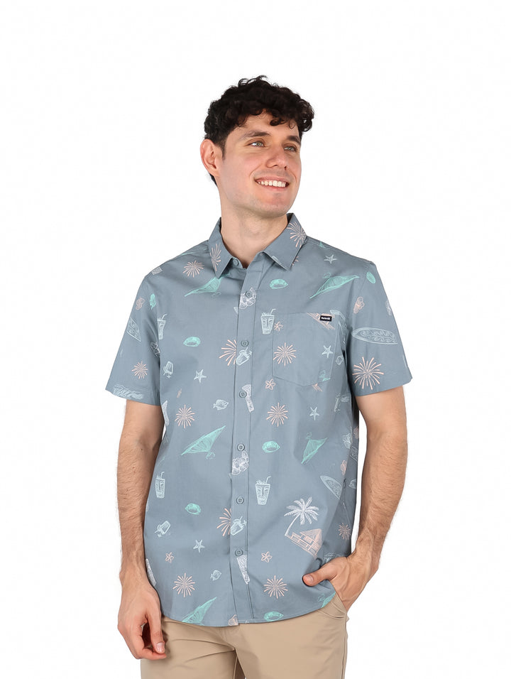 Hombre vistiendo camisa de manga corta color gris con estampado tropical de surf.