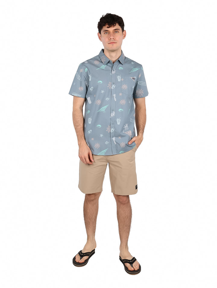 Hombre vistiendo camisa de manga corta color gris con estampado tropical de surf.