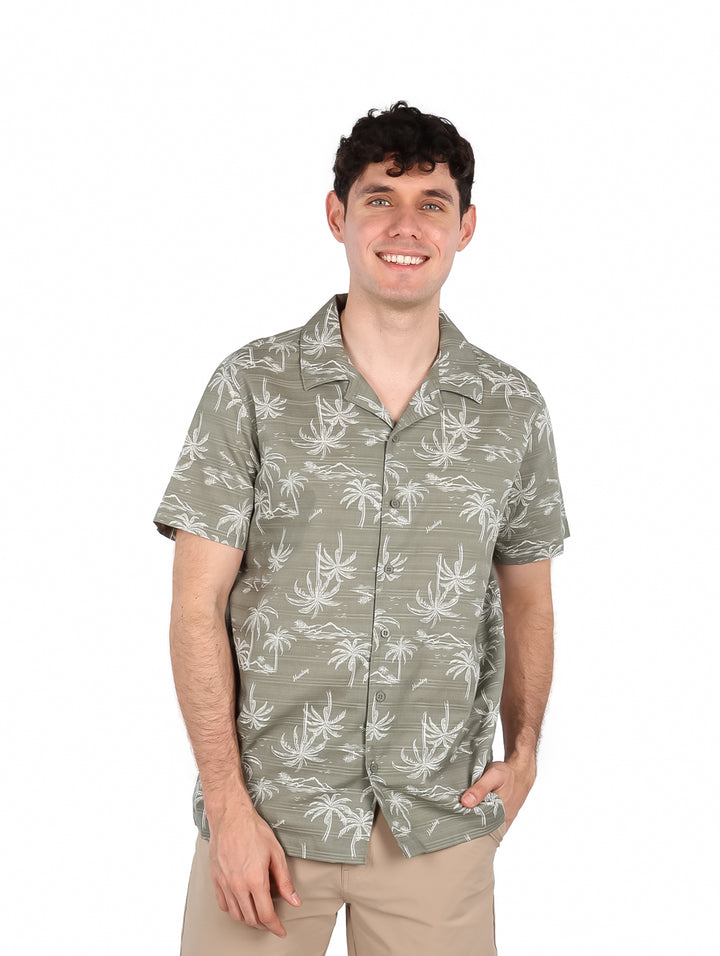 Hombre vistiendo una camisa de manga corta color verde iguana con estampado blanco de palmeras.