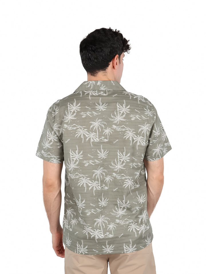 Hombre vistiendo una camisa de manga corta color verde iguana con estampado blanco de palmeras.
