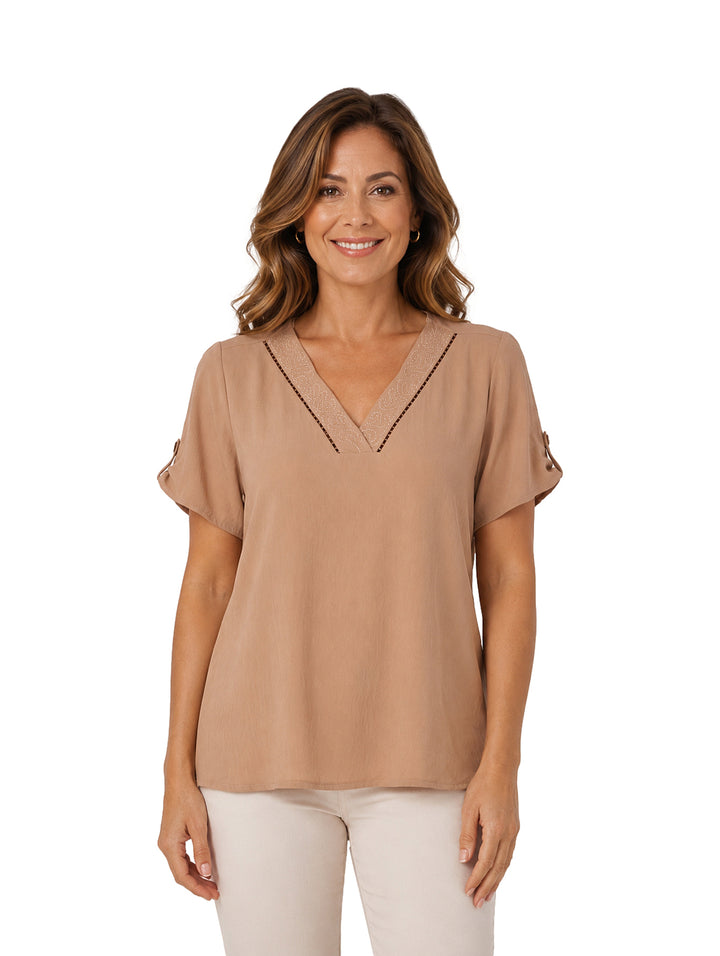 Mujer vistiendo una blusa color beige con cuello en V y detalles decorativos en marrón.