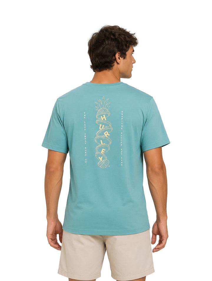 Hombre vistiendo playera de manga corta color verde azulado marca Hurley y shorts beige.