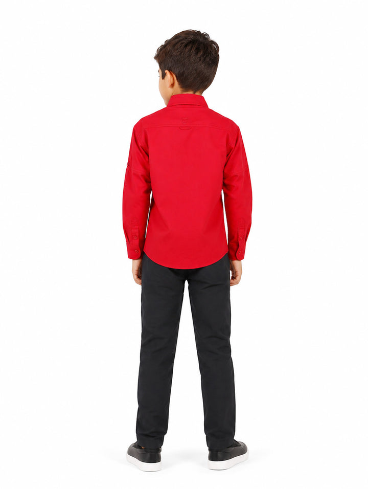 Niño vistiendo una camisa de manga larga color rojo intenso con bolsillos frontales y cuello.