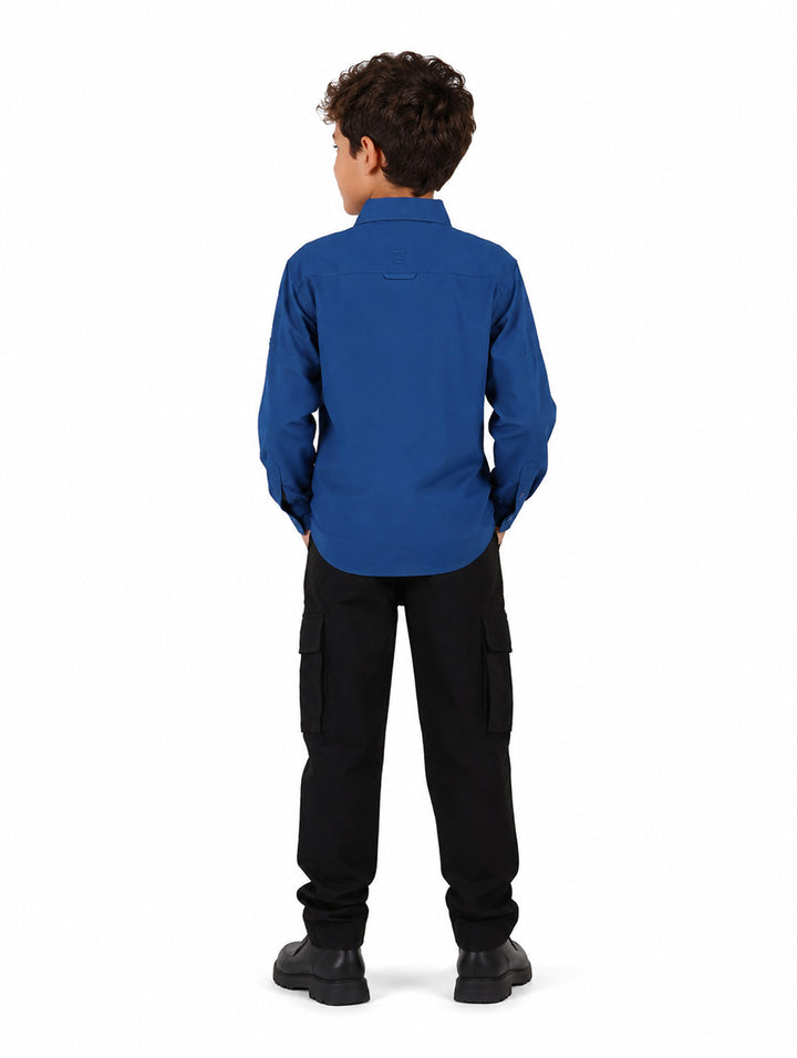 Nino vistiendo una camisa azul de manga larga estilo outdoor con bolsillos frontales.
