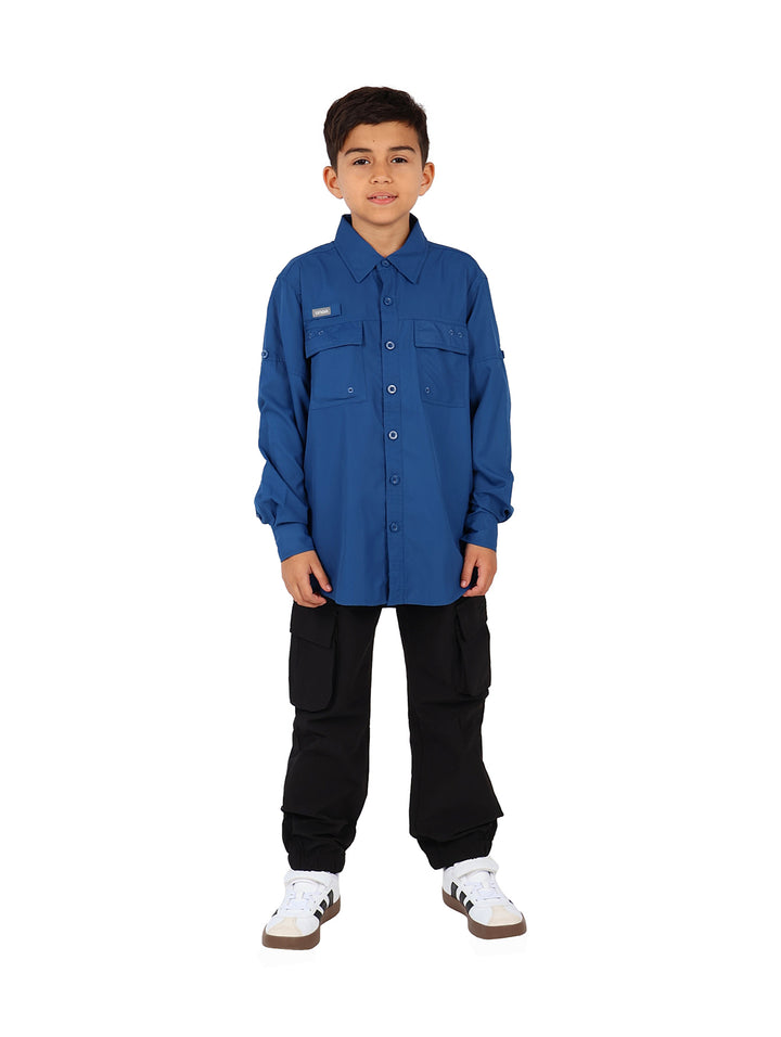 Nino vistiendo una camisa azul de manga larga estilo outdoor con bolsillos frontales.