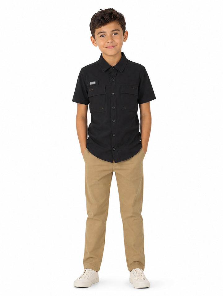 Niño vistiendo una camisa outdoor de color negro con manga corta y bolsillos frontales.