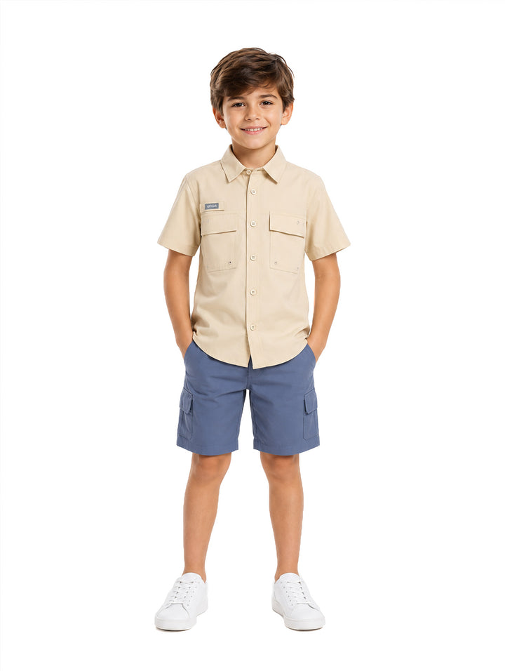 Niño vistiendo una camisa outdoor de manga corta color beige con bolsillos frontales.