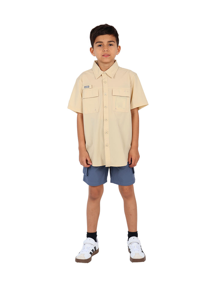 Niño vistiendo una camisa outdoor de manga corta color beige con bolsillos frontales.