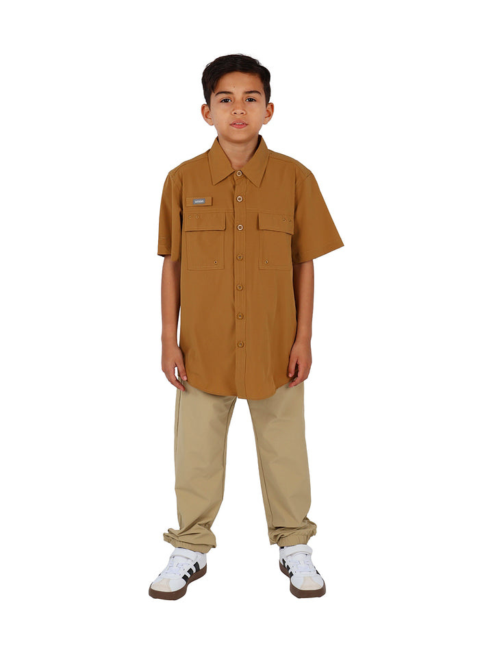 Niño vistiendo una camisa outdoor de manga corta color marrón con bolsillos frontales y botones.