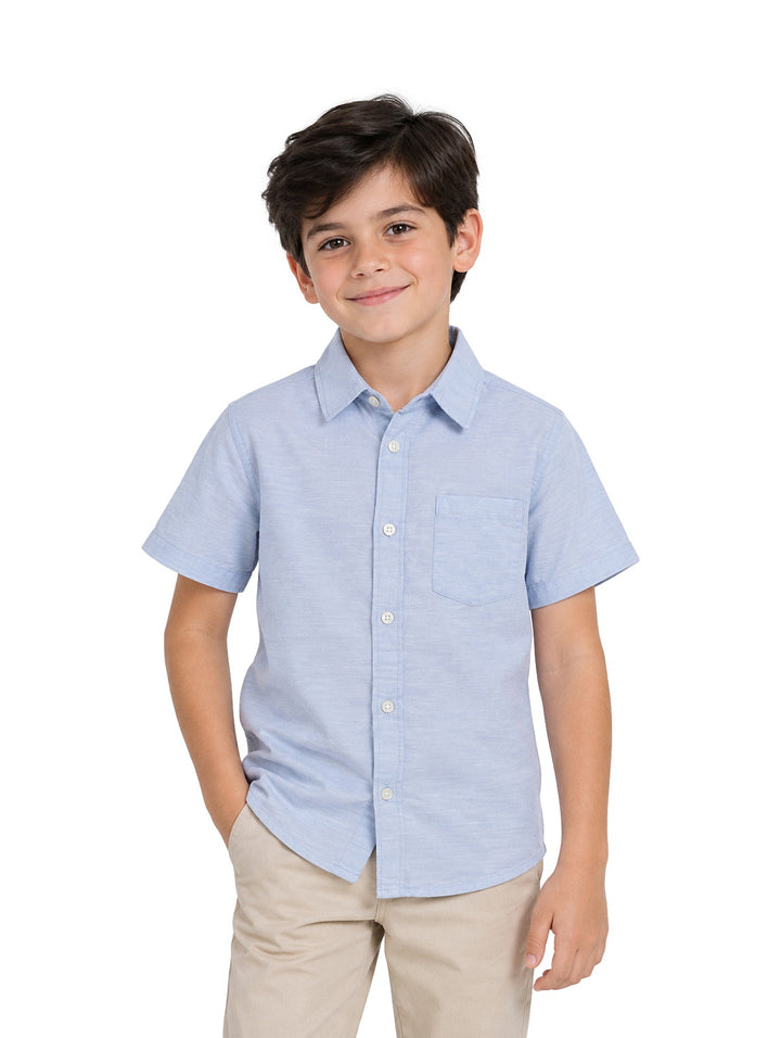 Niño vistiendo una camisa de lino color celeste de manga corta con botones y un bolsillo frontal.