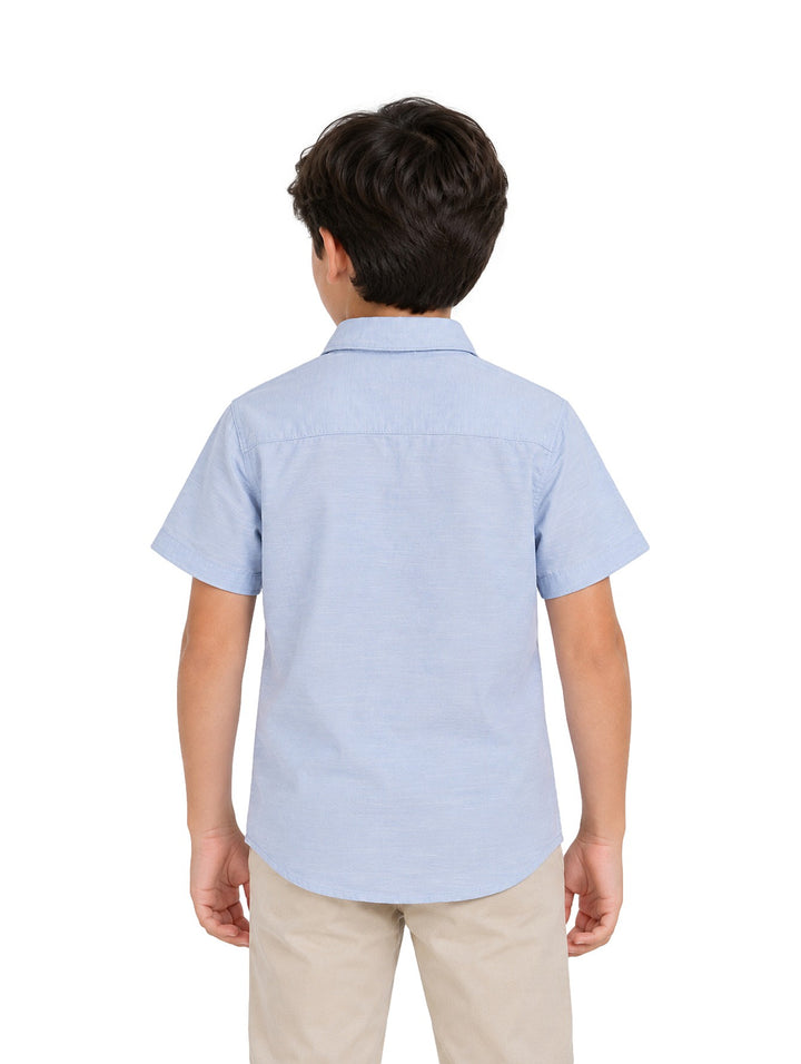 Niño vistiendo una camisa de lino color celeste de manga corta con botones y un bolsillo frontal.