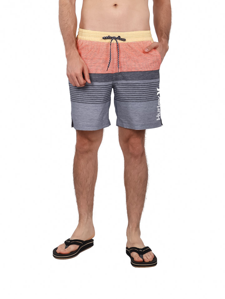 Hombre usando traje de baño Hurley color gris y naranja con rayas horizontales.