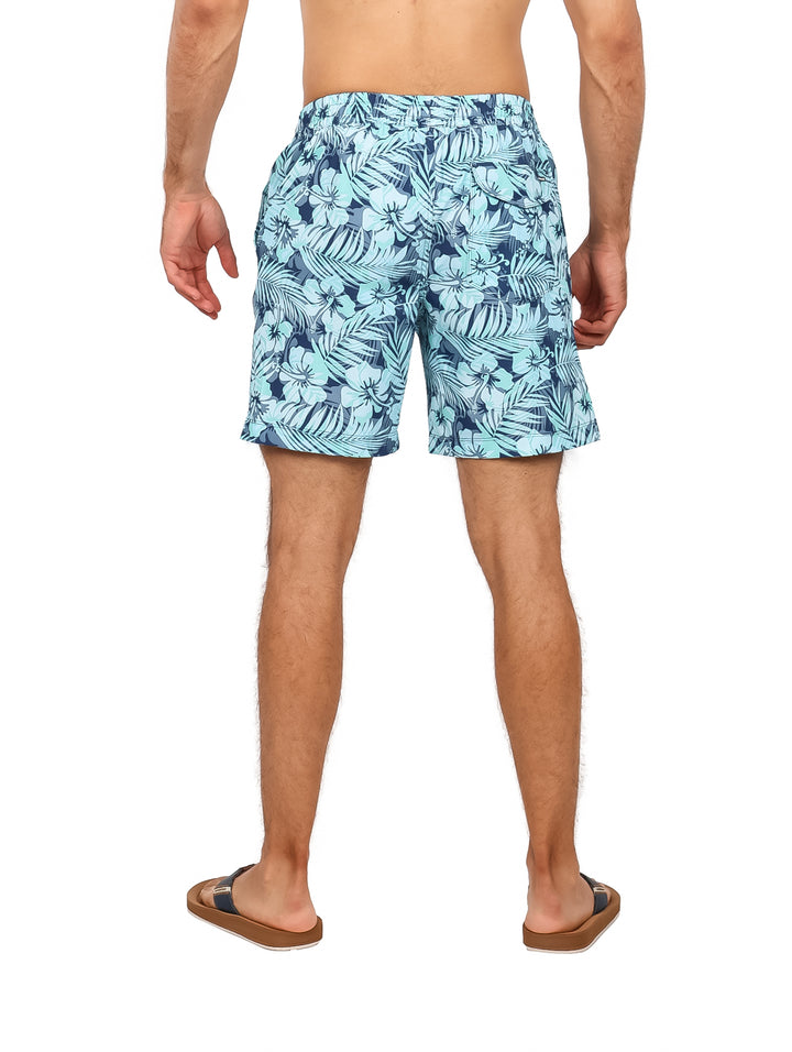 Hombre vistiendo traje de baño Hurley azul con estampado tropical de hojas.