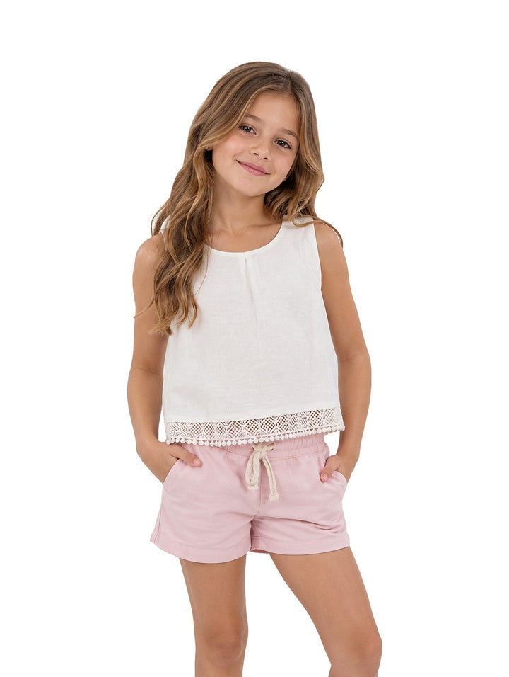 Niña vistiendo camiseta Mayoral color crudo sin mangas con detalle de encaje en el borde inferior.