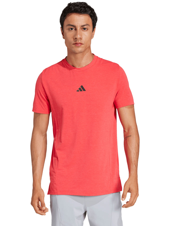 Hombre vistiendo una playera Adidas de color Pure Ruby con logo pequeño en el pecho y cuello redondo.