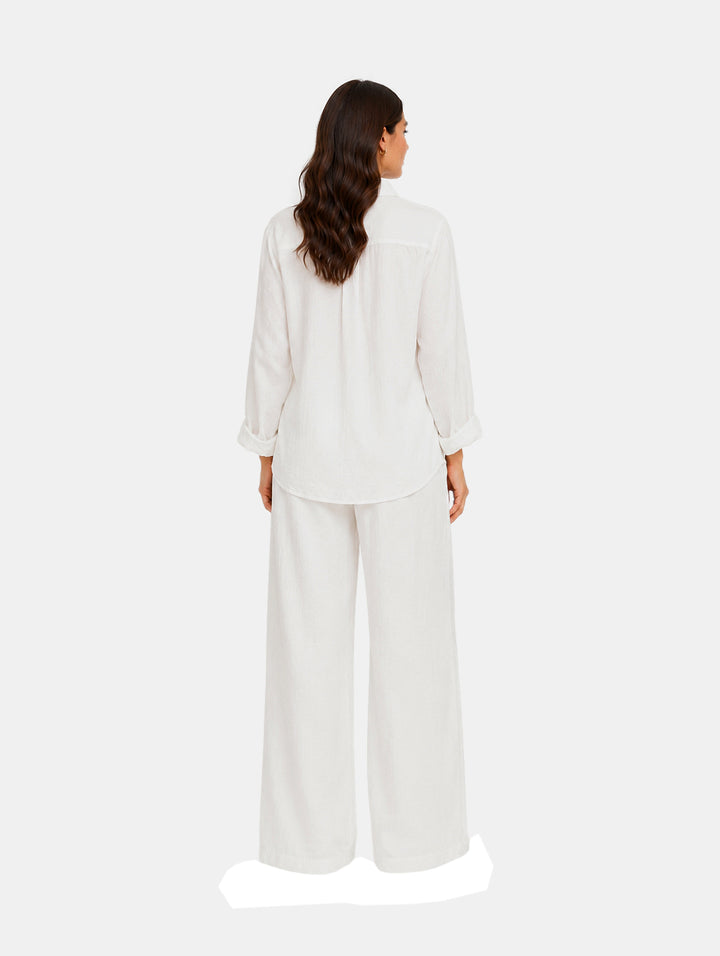 Mujer vistiendo un conjunto de dos piezas color blanco compuesto por camisa y pantalón de pierna ancha.