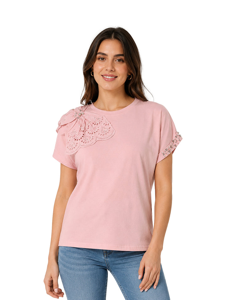 Mujer vistiendo camiseta rosa de manga corta con detalle de encaje en el hombro y jeans azules.
