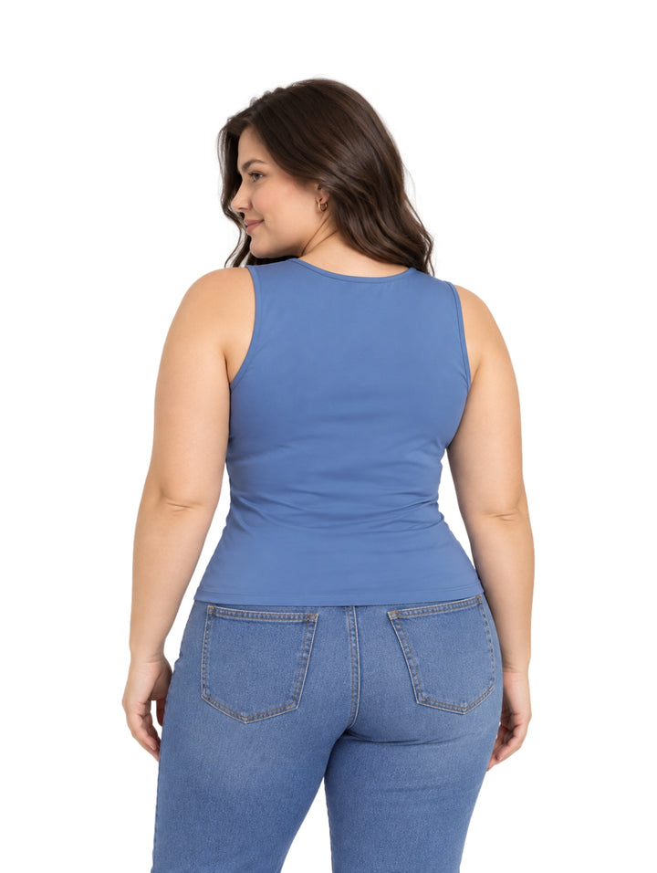 Mujer vistiendo una blusa azul sin mangas y pantalones de mezclilla sobre fondo blanco.