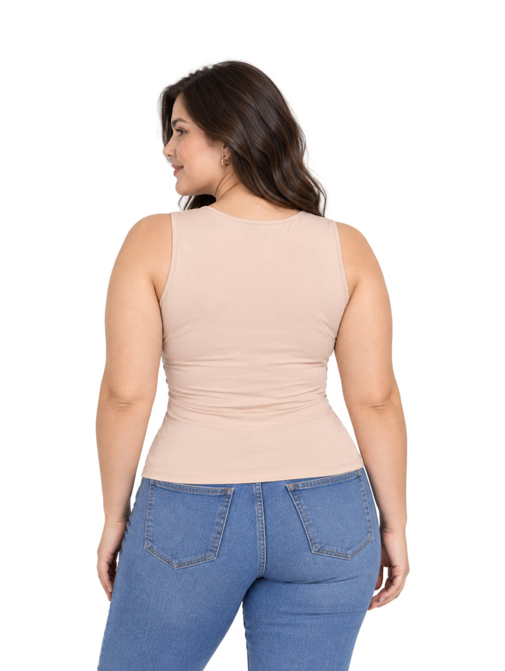 Mujer vistiendo una blusa sin mangas color champagne ajustada y pantalones de mezclilla azules.